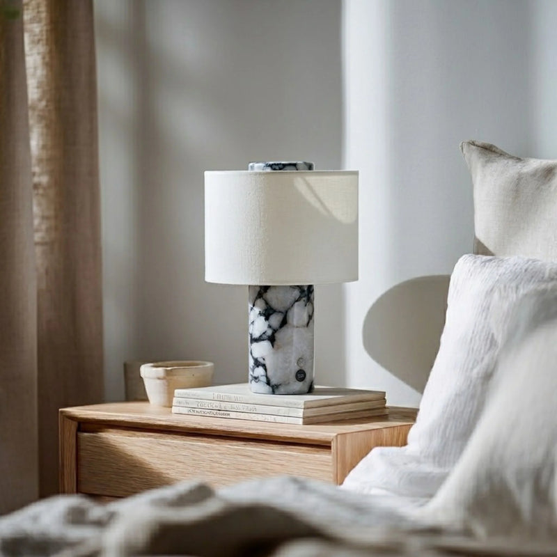 Nighstand with lamp and books next to a bed in a bedroom setting