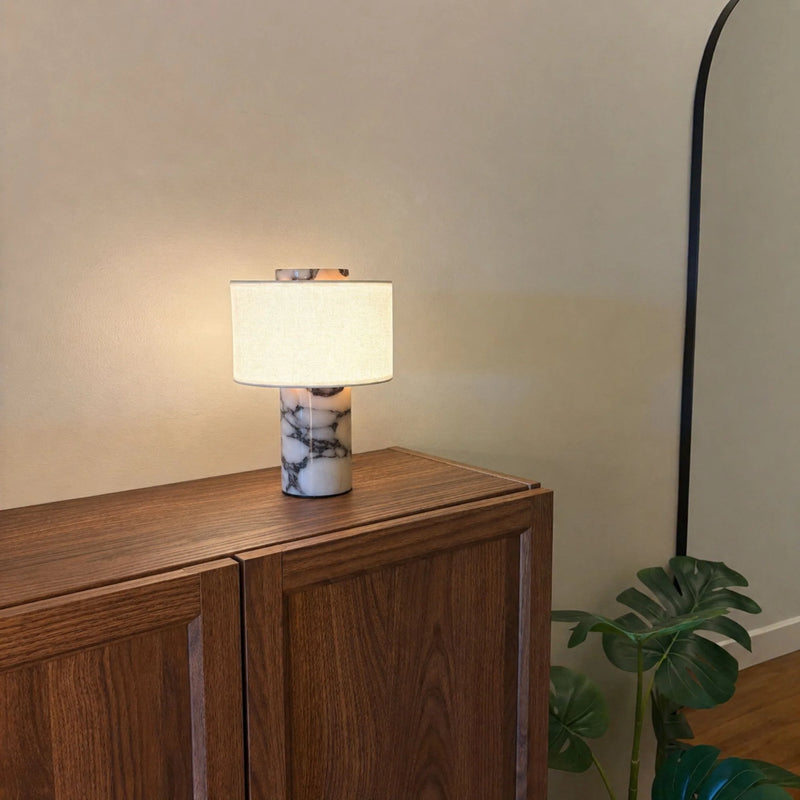 Table lamp with marble base on a wooden cabinet next to a plant